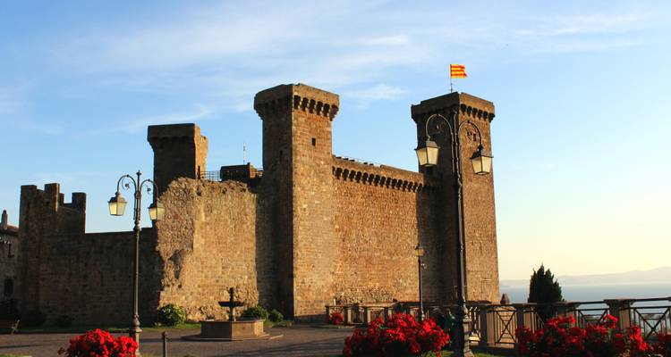 Medieval stone castle with crenellated towers flying a small flag under evening light