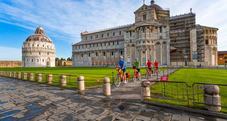 Radfahrer fahren an der ikonischen Kathedrale und dem Baptisterium von Pisa innerhalb der Piazza dei Miracoli vorbei.