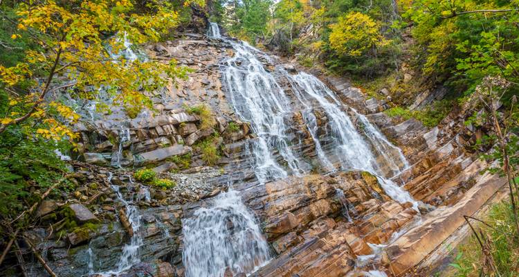 Ein Wasserfall, der über felsiges Gelände hinabstürzt, umgeben von üppiger Vegetation.