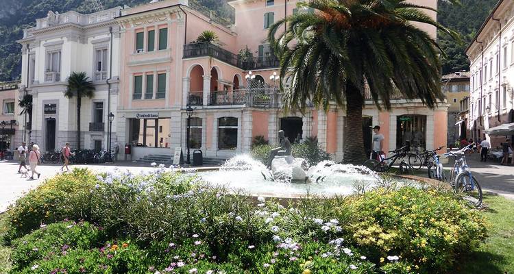 Stadtszene mit einem Brunnen, Palmen und Menschen.