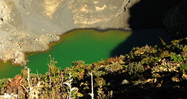 Turquoise lake within a volcanic crater, casting shadows.
