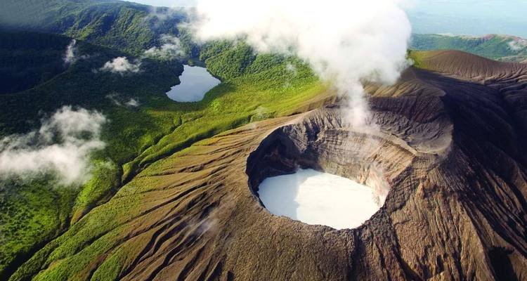 Aerial view of volcanic crater emitting steam with verdant surroundings.