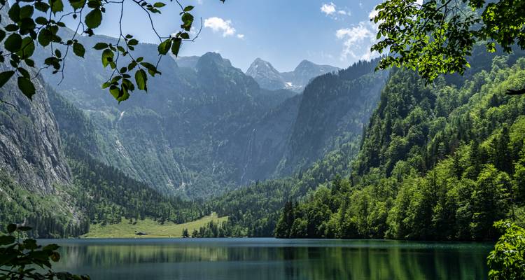 Makelloses Alpensee, das steile, bewaldete Berge und Gipfel unter klarem Sommerhimmel widerspiegelt.