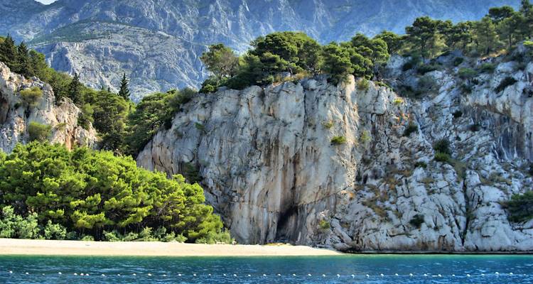Rocky cliffside with pine trees and turquoise sea.