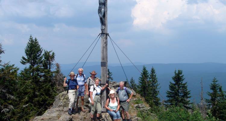 A group of elderly hikers posing by a wooden cross on a mountain.