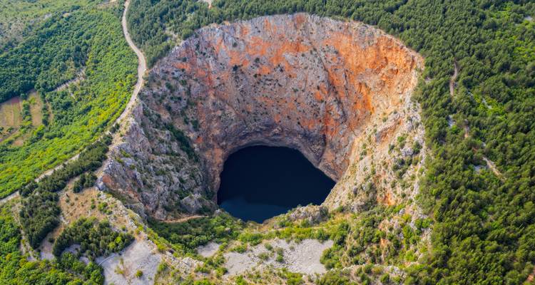 Luchtfoto van een grote ronde zinkgat met een meer op de bodem.