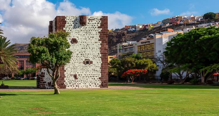 Historic stone tower with white-and-brown facade stands in a green city park.