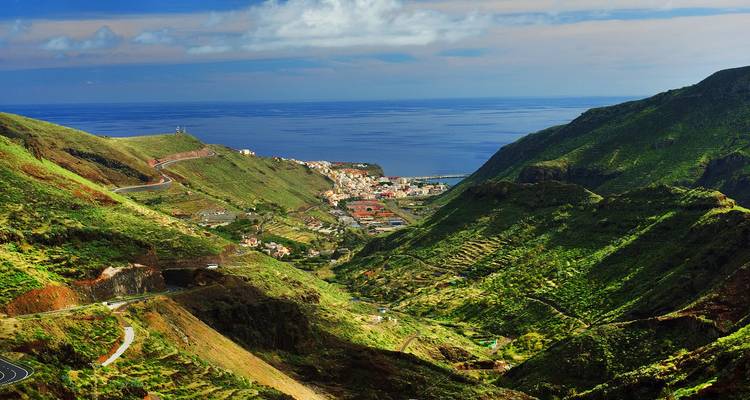 Green terraced valley opens to a seaside town and expansive blue ocean horizon.