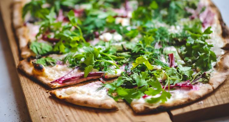 Close-up of a thin-crust pizza with herbs on a wooden board.