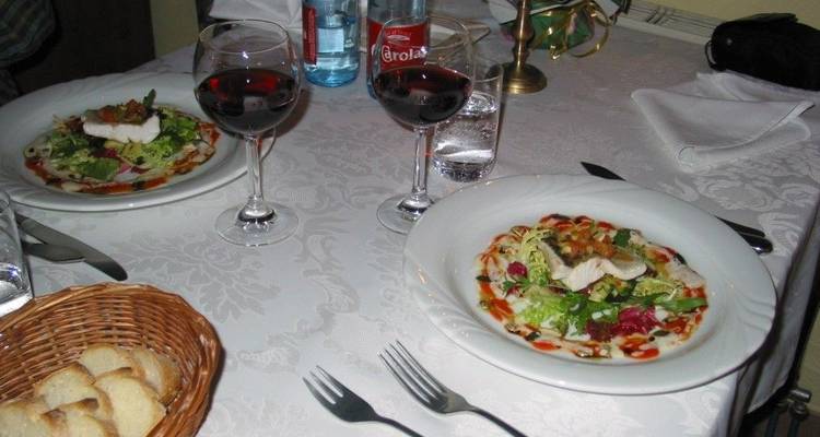 Table de salle à manger avec des assiettes de nourriture, des verres de vin et un panier de pain.