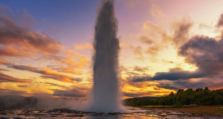 Ausbrechender Geysir vor einem farbenprächtigen Sonnenuntergangshimmel.