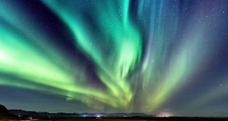 Helle Polarlichter über einer dunklen Landschaft.