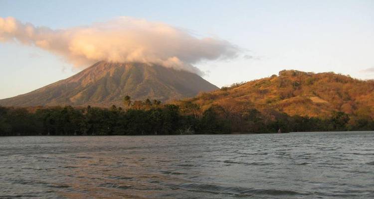Volcano with clouds at sunset over water.