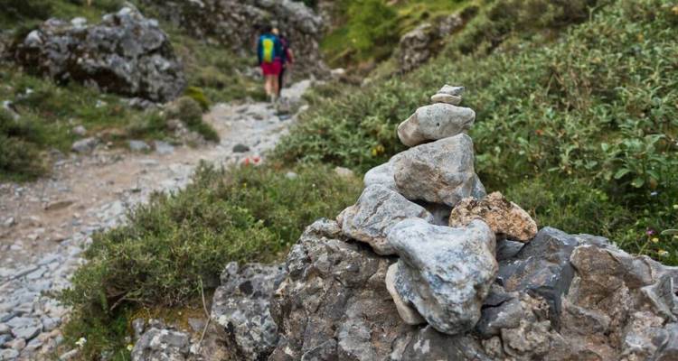 Wandelaar die door een rotsachtig landschap loopt met steenmannetjes en groen.