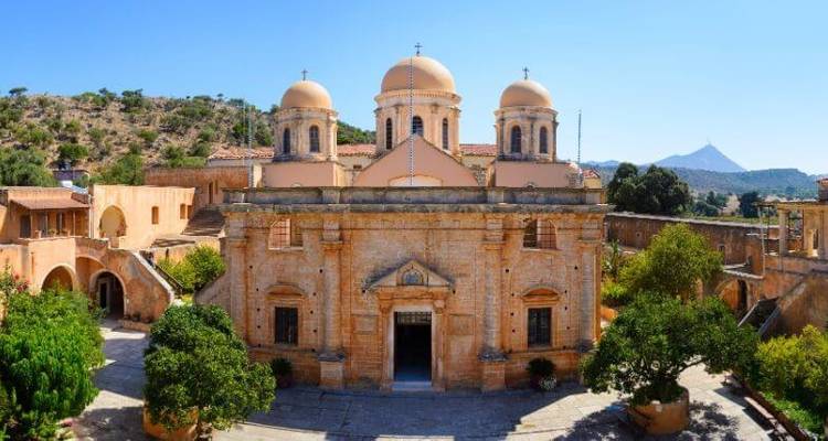 Een historisch klooster met grote koepels omgeven door groen en bergen op de achtergrond.