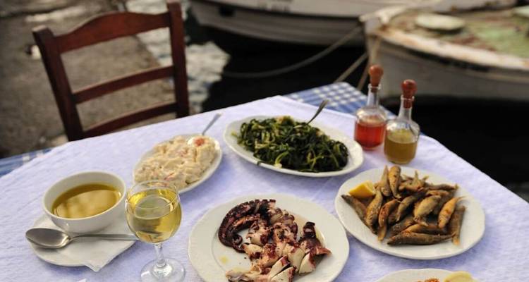 Tafel met borden traditioneel eten, inclusief zeevruchten en wijn, aan het water.