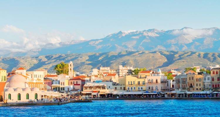 Kleurrijke waterkant met architectuur onder een blauwe hemel met bergen op de achtergrond.