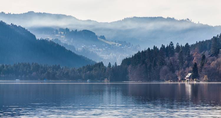 Colinas cubiertas de niebla reflejándose en el agua de un lago.