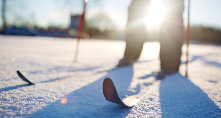 Gros plan sur des skis dans la neige avec la lumière du soleil en arrière-plan.