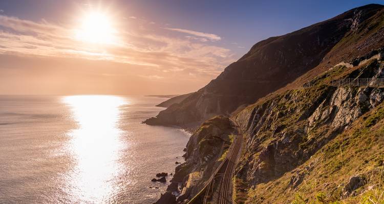 Scenic view of a coastline with railway tracks and a setting sun.
