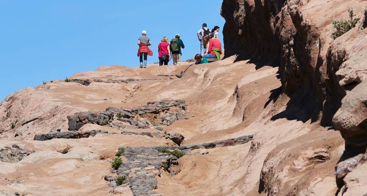 Gruppe von Menschen, die auf felsigem Gelände bei klarem blauem Himmel wandern.