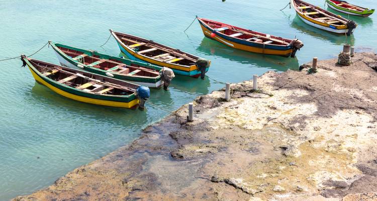 Row of small colorful wooden fishing boats moored on calm turquoise water beside a rocky quay.