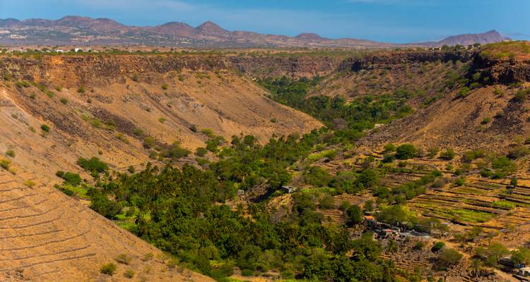 Arid valley with patchwork of terraced fields and sparse greenery under a hazy sky.