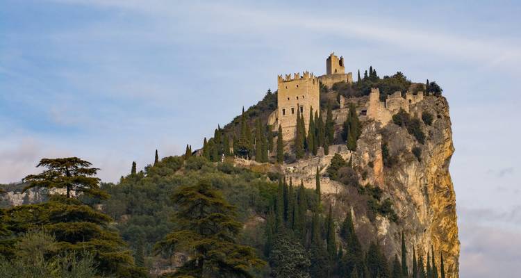 Historische Burgruine auf einem steilen Felsen, umgeben von Zypressen.
