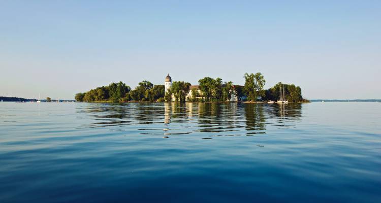 Île isolée avec des bâtiments entourée d'eaux calmes.