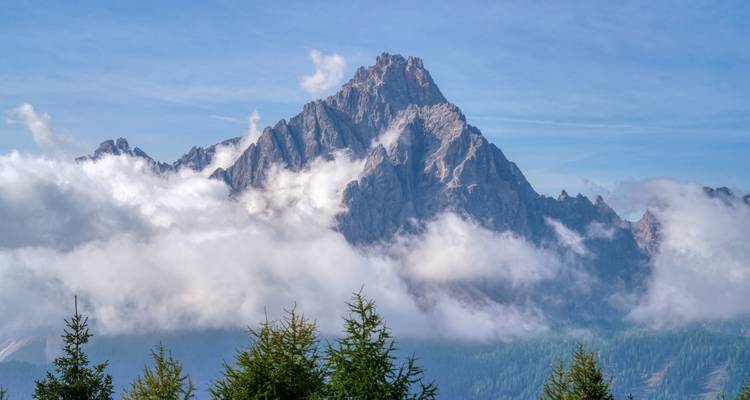 Mountain peak rising through clouds with a blue sky.