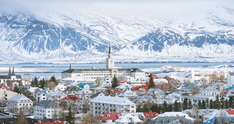 Winterpanorama der farbenfrohen Dächer Reykjaviks vor schneebedeckten Bergen und dem Meer.