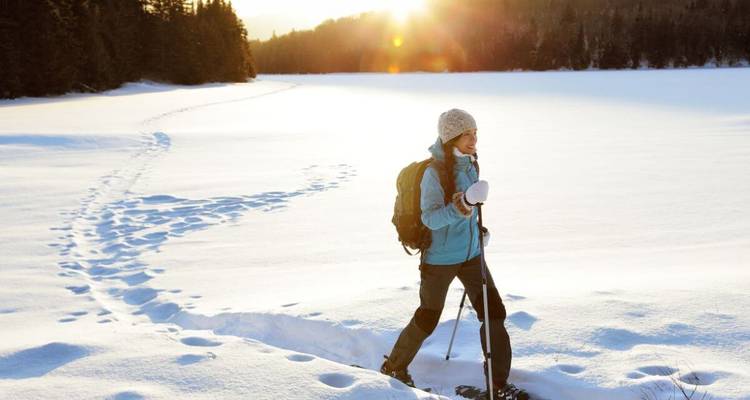 Une personne faisant de la raquette sur un paysage enneigé avec du soleil.