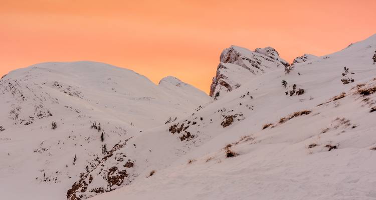 Puesta de sol ilumina montañas nevadas con un cielo naranja-rosado.