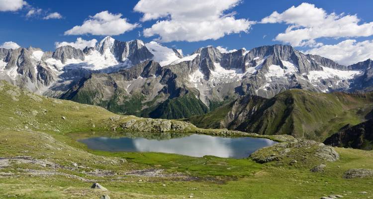 Hochalpiner Bergsee, der die verschneiten Gipfel der Ortler-Cevedale-Gruppe unter leuchtenden Wolken spiegelt.