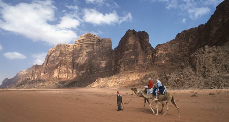 Des gens à dos de chameaux dans un paysage désertique avec des montagnes rocheuses.