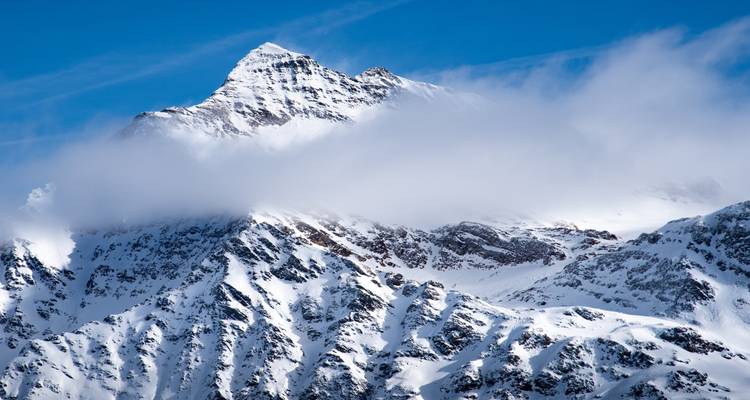 Montagne enneigée avec des nuages recouvrant délicatement le sommet.