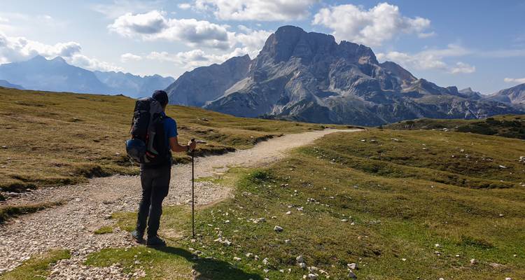 Un excursionista parado en un sendero contemplando amplias vistas montañosas.