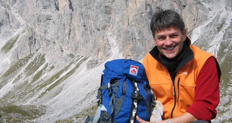 Un homme avec un sac à dos souriant avec un arrière-plan de montagne rocheuse.