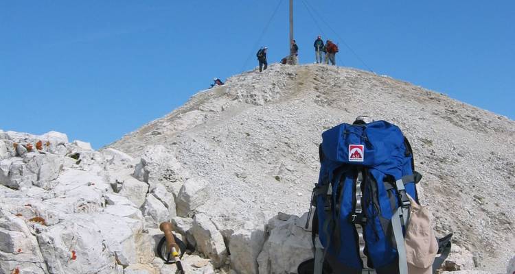 Mochila colocada en terreno rocoso con excursionistas en la cumbre.
