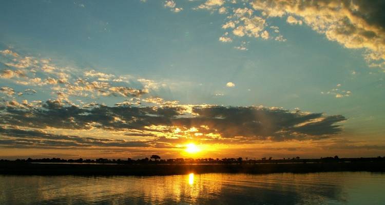 Lebendiger Sonnenuntergang über einem breiten ruhigen Fluss mit Spiegelungen von orangefarbenem Licht und verstreuten Wolken.