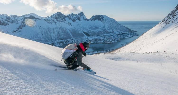 Skieur effectuant un virage sur une pente raide enneigée avec des montagnes au loin.