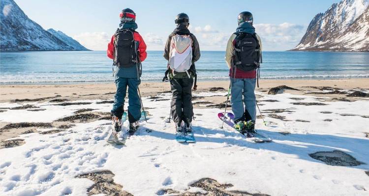 Des skieurs sur une plage enneigée face à l'océan.