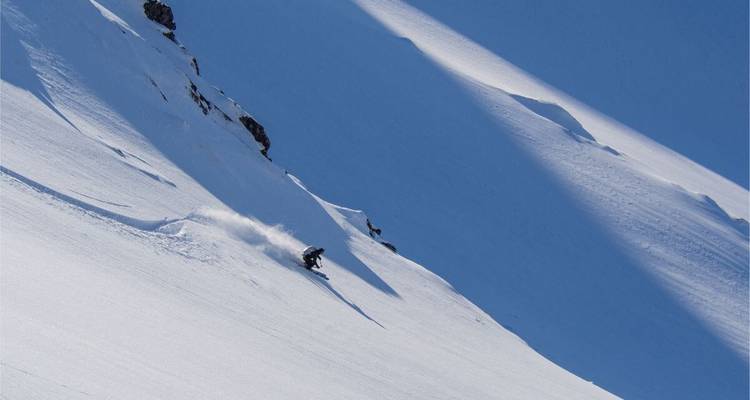 Skieur naviguant sur une pente raide avec de la neige poudreuse.