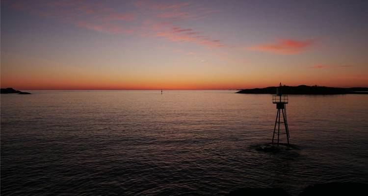 Mer calme au coucher du soleil avec des traces de nuages roses et une bouée solitaire.