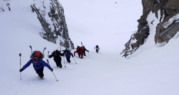 Menschen, die einen verschneiten Hang zwischen felsigen Klippen hinaufwandern.