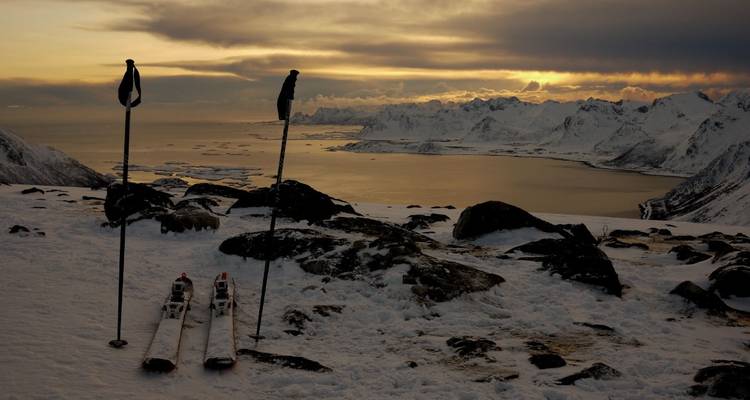 Skistöcke und Skier mit einem Sonnenuntergang über schneebedeckten Bergen.