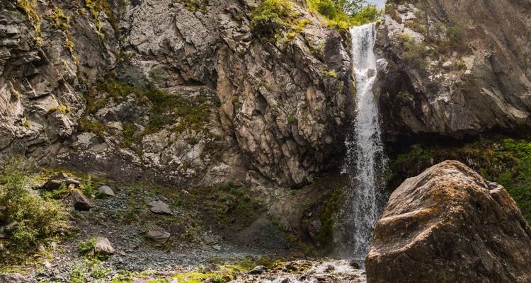 Een waterval die naar beneden stroomt langs een rotsachtige klif omgeven door groen.
