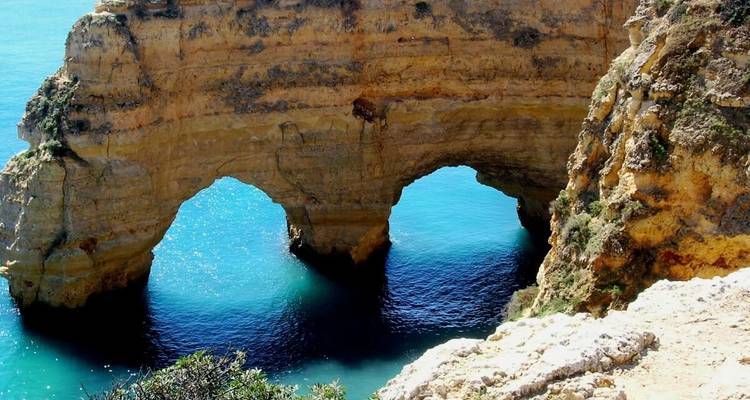 Natural rock arch formations above a bright blue sea.