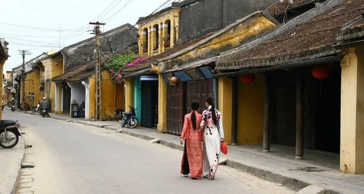 Twee vrouwen in traditionele Vietnamese kledij die door een historische straat lopen.
