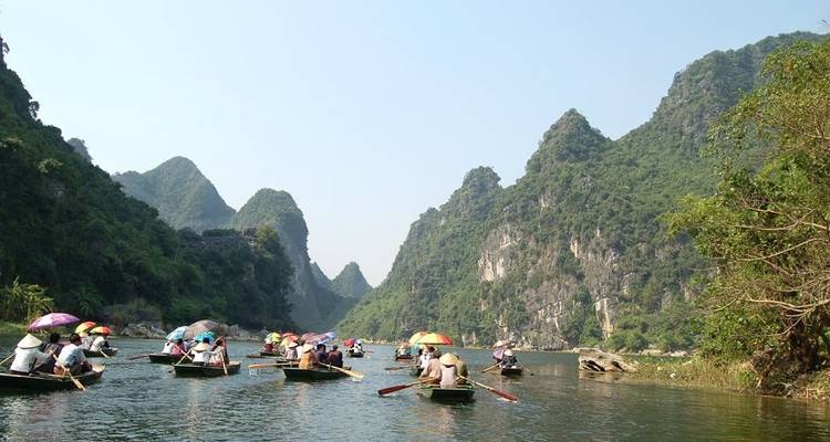 Toeristen in roeiboten die peddelen door een rivier omgeven door torenhoge kalkstenen kliffen.